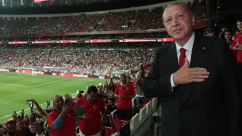 AK Parti'nin Milli Takım için hazırladığı 'Siz Hepiniz Biz Türkiye' marşının klibinden bir kare. Klibin Cumhurbaşkanı Erdoğan, Togg ve savunma sanayii ürünlerini içerdiği görülüyor.